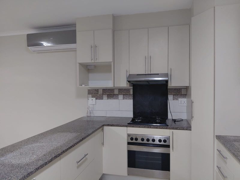 Modern kitchen featuring neutral cabinetry, granite countertops, built-in gas hob, electric oven, extractor fan, and a wall-mounted air conditioning unit.