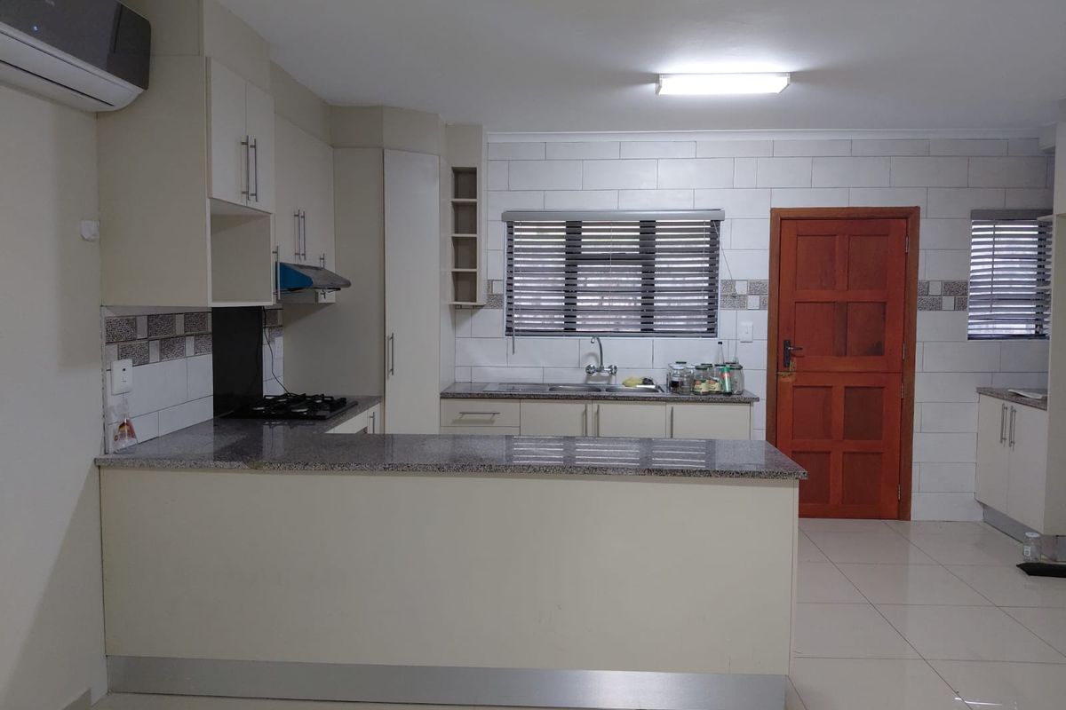 A functional kitchen featuring granite countertops, built-in cabinetry, a gas hob with extractor fan, and tiled splashbacks, offering a clean and practical workspace.