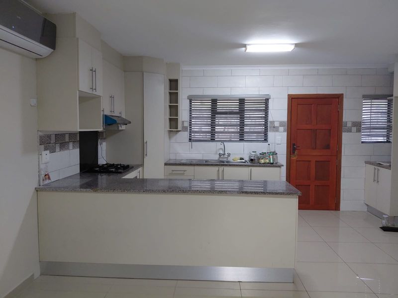 A functional kitchen featuring granite countertops, built-in cabinetry, a gas hob with extractor fan, and tiled splashbacks, offering a clean and practical workspace.
