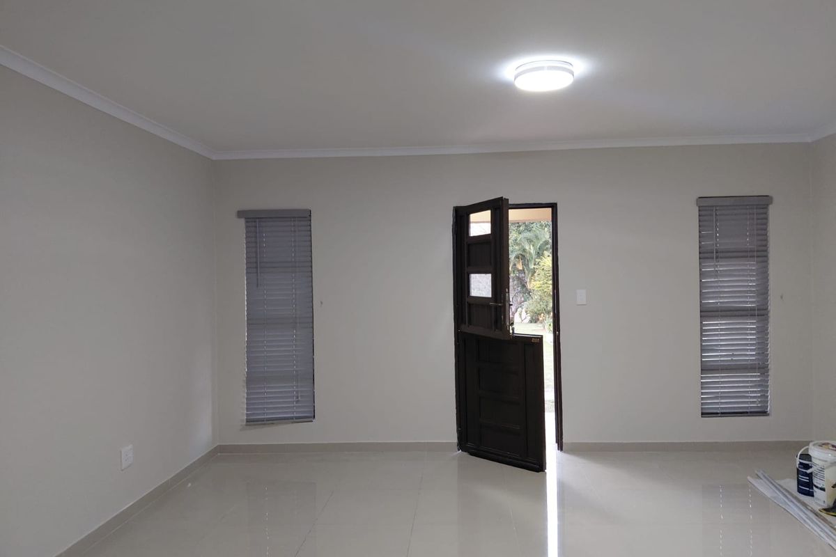 A bright, open-plan living area featuring neutral tiled flooring, modern venetian blinds, and a classic stable-style entrance door.