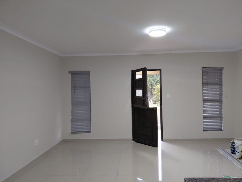 A bright, open-plan living area featuring neutral tiled flooring, modern venetian blinds, and a classic stable-style entrance door.