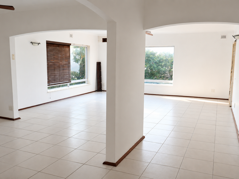 Spacious, light-filled open-plan living area featuring neutral tiled flooring, arched architectural details, and large windows with fitted blinds.