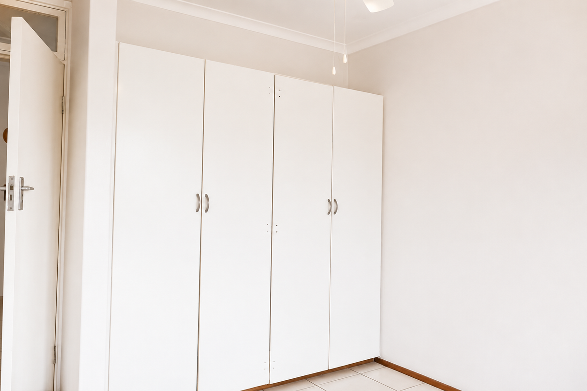 A clean, empty bedroom featuring white built-in wardrobes, tiled flooring, and a ceiling fan, offering a neutral canvas for personalization.