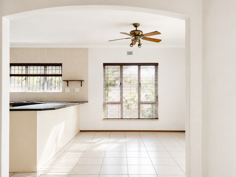 An empty kitchen featuring tiled flooring, a central island with a dark countertop, and a ceiling fan, viewed through a classic archway.