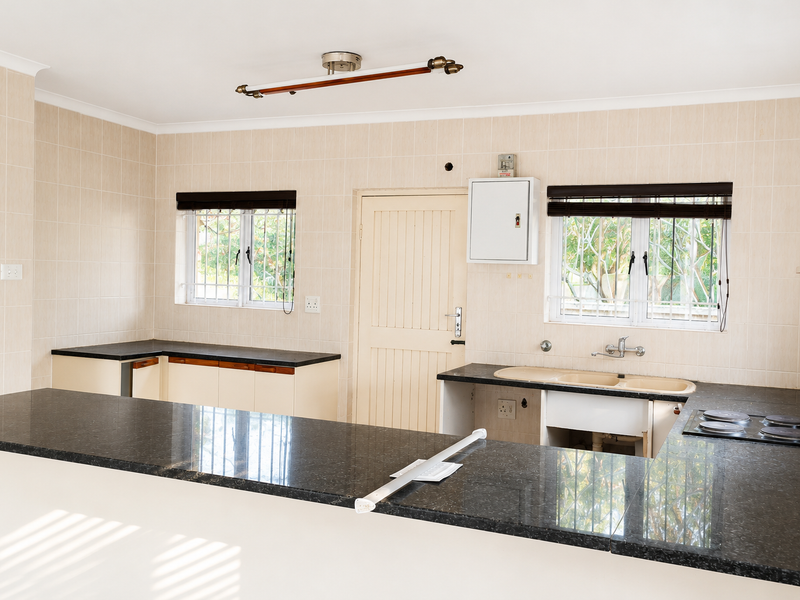 A functional kitchen featuring granite countertops, a built-in electric hob, and double basin sink, with tiled walls and security bars on the windows.