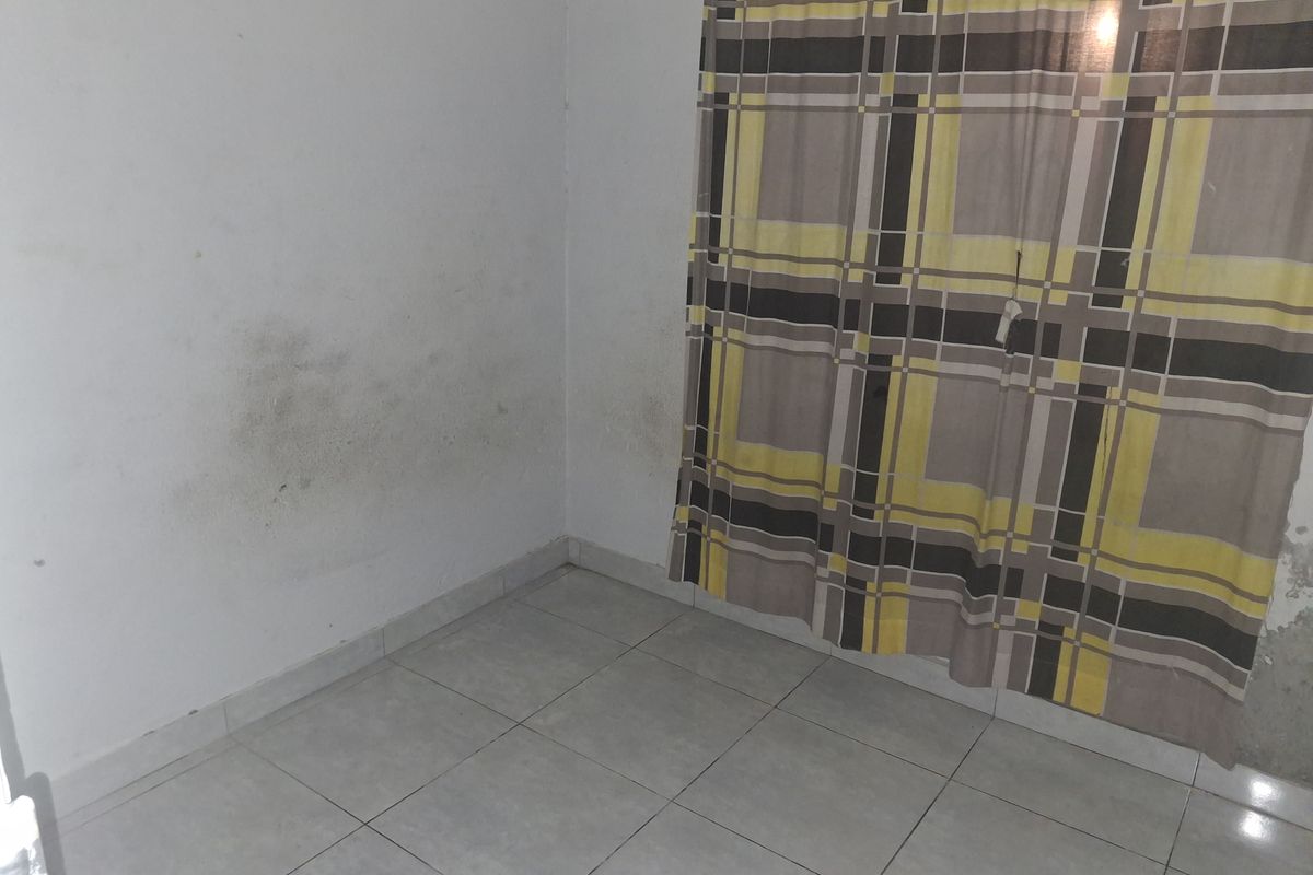 An empty bedroom featuring tiled flooring and visible wall staining, requiring maintenance and cosmetic updates.