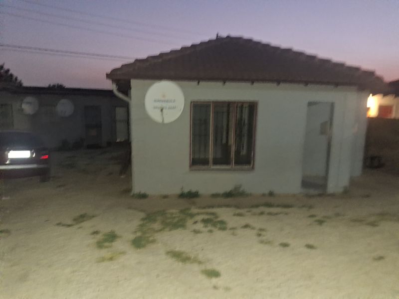 Front view of a single-story residential house with a tiled roof and security bars on the windows, set on an unpaved lot.
