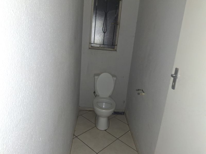 A compact, functional guest toilet featuring tiled flooring and a small window with security bars.