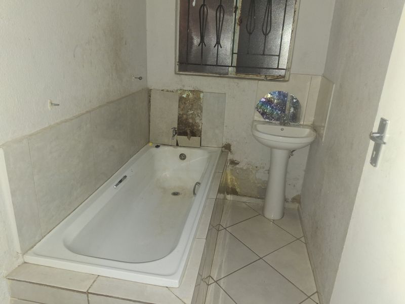 A small bathroom featuring a built-in bathtub and pedestal basin, currently requiring significant maintenance and renovation due to visible wall damage and wear.