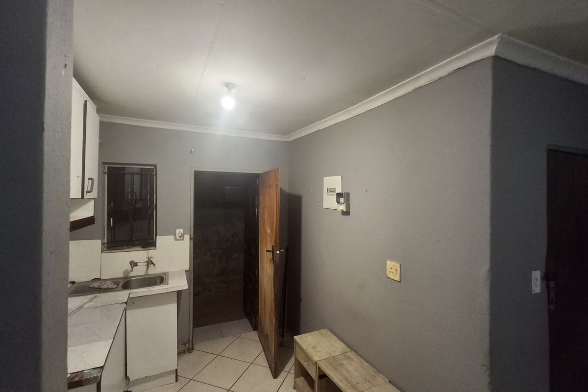 A compact, empty kitchen area featuring tiled flooring, basic built-in cabinetry, and a sink, offering a functional space ready for modernization.
