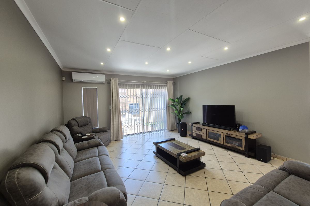 A well-maintained living room featuring tiled flooring, recessed downlighting, and a split-system air conditioner, with direct access to the exterior via a sliding door.