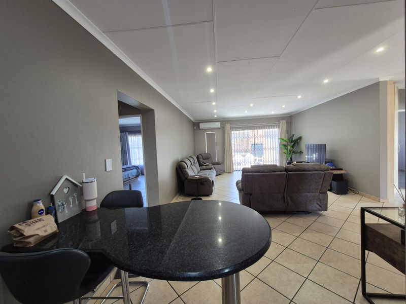 Spacious open-plan living area featuring tiled flooring, recessed lighting, an air conditioning unit, and a granite breakfast bar leading to a sliding glass door.