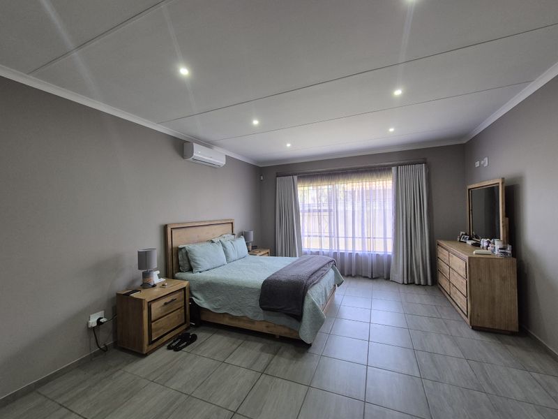 Spacious bedroom featuring neutral wall tones, tiled flooring, recessed lighting, and a wall-mounted air conditioning unit.