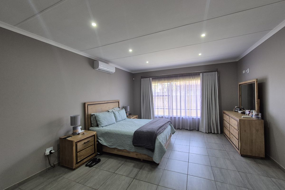 Spacious bedroom featuring neutral wall tones, tiled flooring, recessed lighting, and a wall-mounted air conditioning unit.