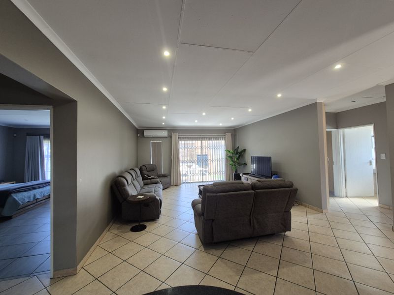 Spacious living room featuring tiled flooring, recessed downlighting, and a sliding glass door with security gate providing access to the exterior.