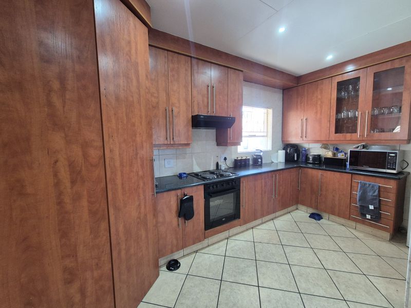 A functional kitchen featuring warm-toned wood cabinetry, dark laminate countertops, built-in oven with gas hob, and tiled flooring.