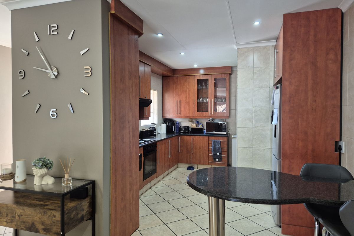 A functional kitchen featuring warm-toned built-in cabinetry, granite countertops, integrated appliances, and tiled flooring, seamlessly connected to the adjacent living area.