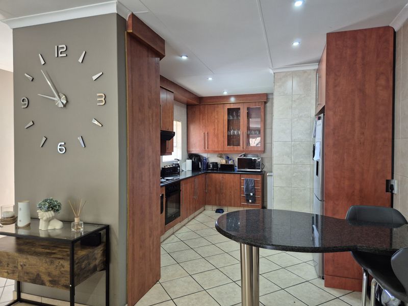 A functional kitchen featuring warm-toned built-in cabinetry, granite countertops, integrated appliances, and tiled flooring, seamlessly connected to the adjacent living area.