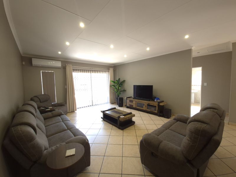 Spacious living room featuring tiled flooring, recessed downlighting, and a split-system air conditioner, with direct access to the exterior via a sliding glass door.