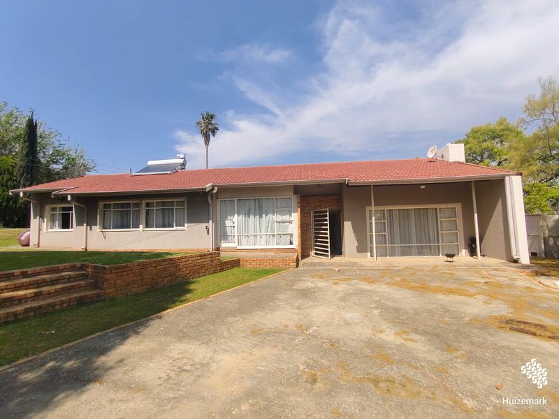 Rear view of a single-story house featuring a tiled roof, solar water heater, concrete driveway, and brick retaining wall in the garden area.