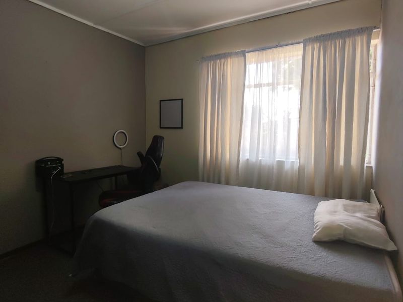 A functional bedroom featuring neutral wall tones, carpeted flooring, and a window with curtains providing natural light.