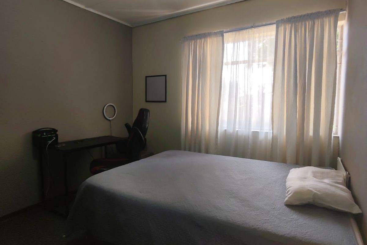 A functional bedroom featuring neutral wall tones, carpeted flooring, and a window with curtains providing natural light.