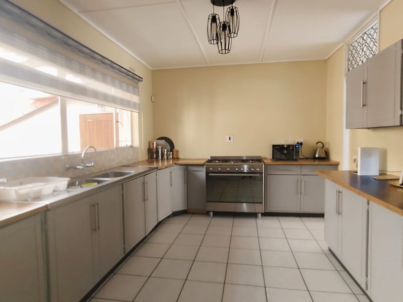 A functional kitchen featuring grey built-in cabinetry, laminate countertops, a stainless steel gas stove, and tiled flooring with ample workspace.