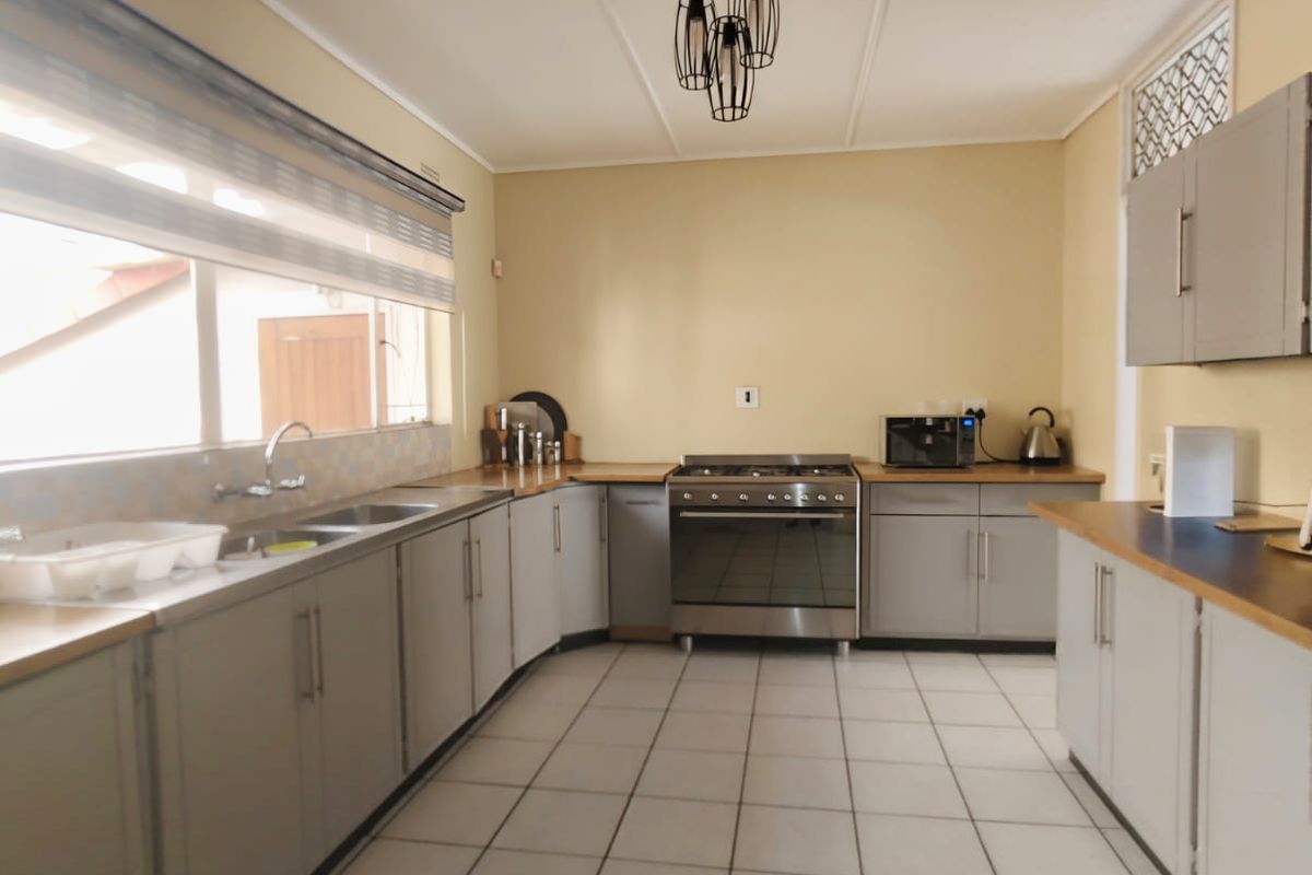 A functional kitchen featuring grey built-in cabinetry, laminate countertops, a stainless steel gas stove, and tiled flooring with ample workspace.