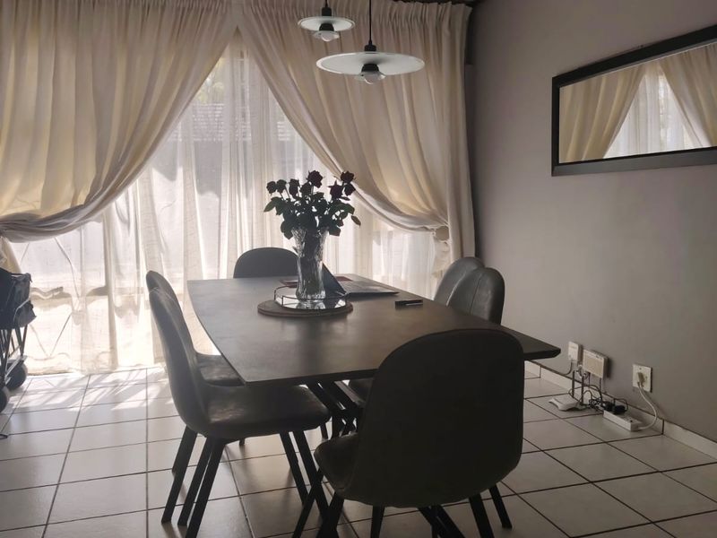 A dining room featuring tiled flooring, dual pendant lighting, and a large sliding glass door with curtains providing natural light.