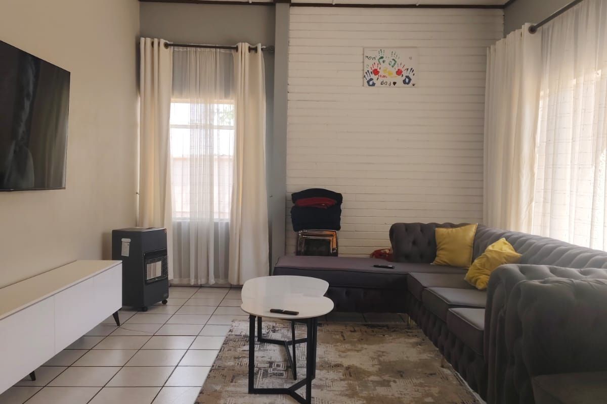 A living room featuring tiled flooring, timber wall paneling, and an exposed beam ceiling, offering a comfortable and functional space.
