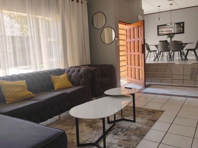 Spacious open-plan living and dining area featuring tiled flooring, a raised dining platform, and a classic timber entrance door.