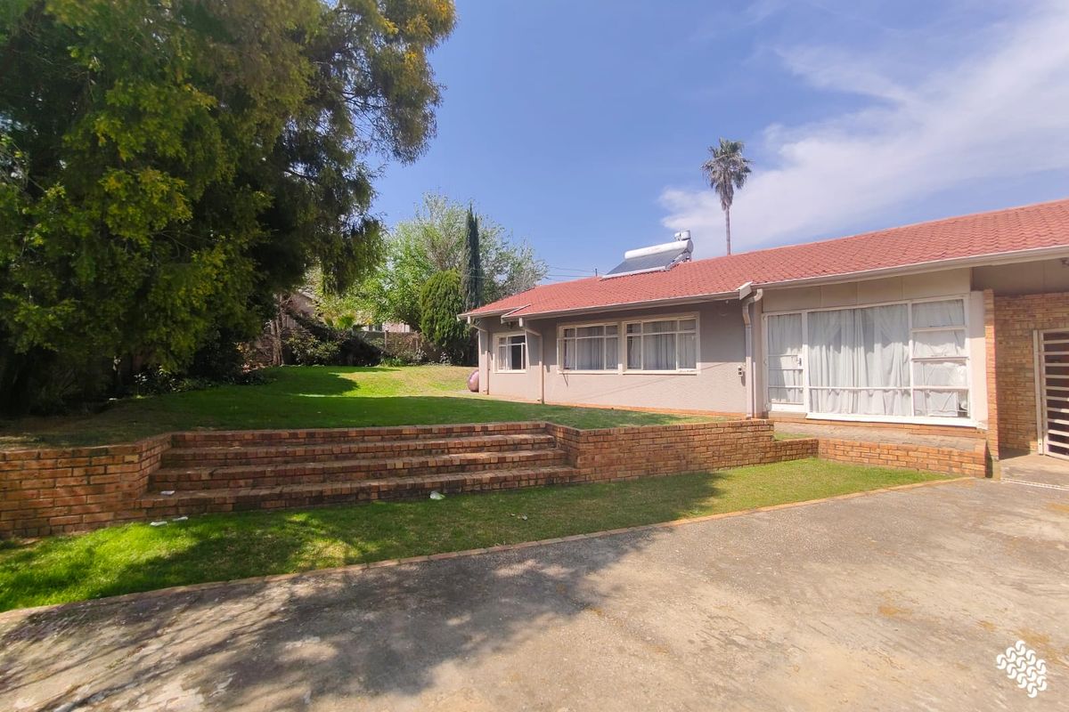 Rear view of the property featuring a brick retaining wall, a spacious lawn, and a tiled roof with a solar water heating system.