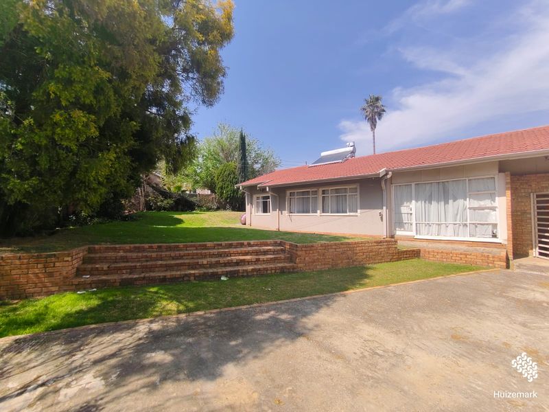 Rear view of the property featuring a brick retaining wall, a spacious lawn, and a tiled roof with a solar water heating system.