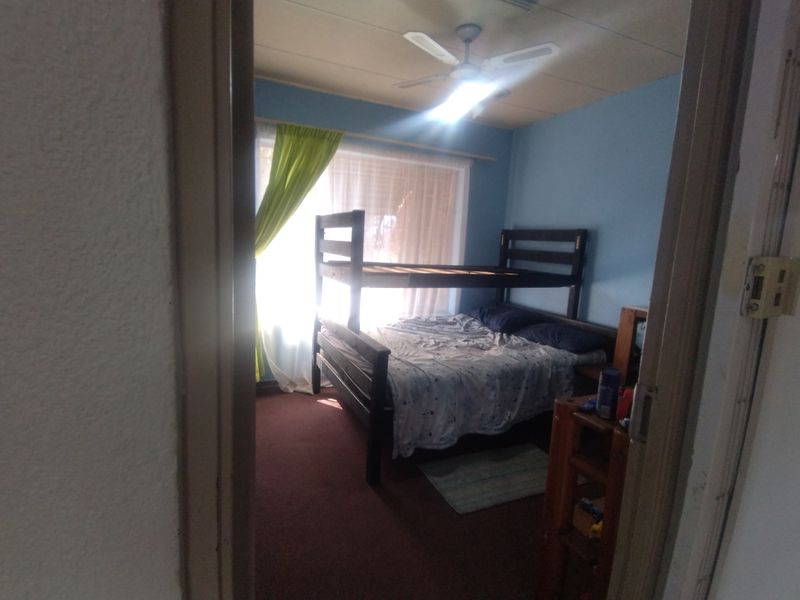 A bedroom featuring carpet flooring and a ceiling fan, viewed from the doorway with natural light entering through the window.