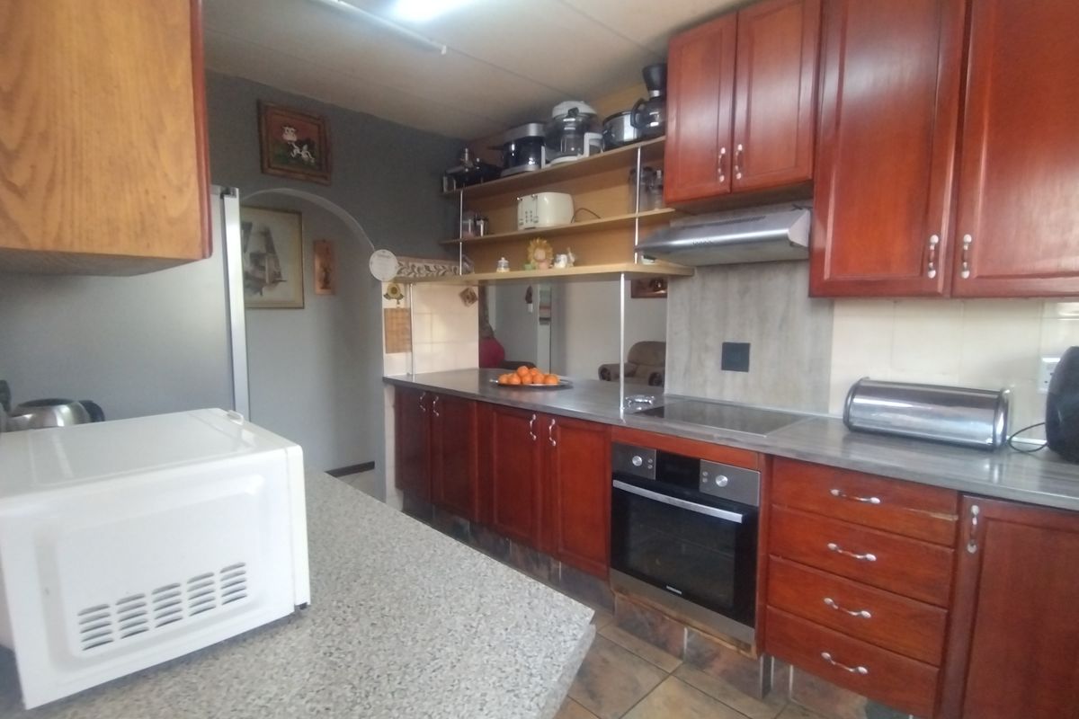 A functional kitchen featuring wooden cabinetry, built-in oven, electric hob, extractor fan, and laminate countertops with tiled flooring.