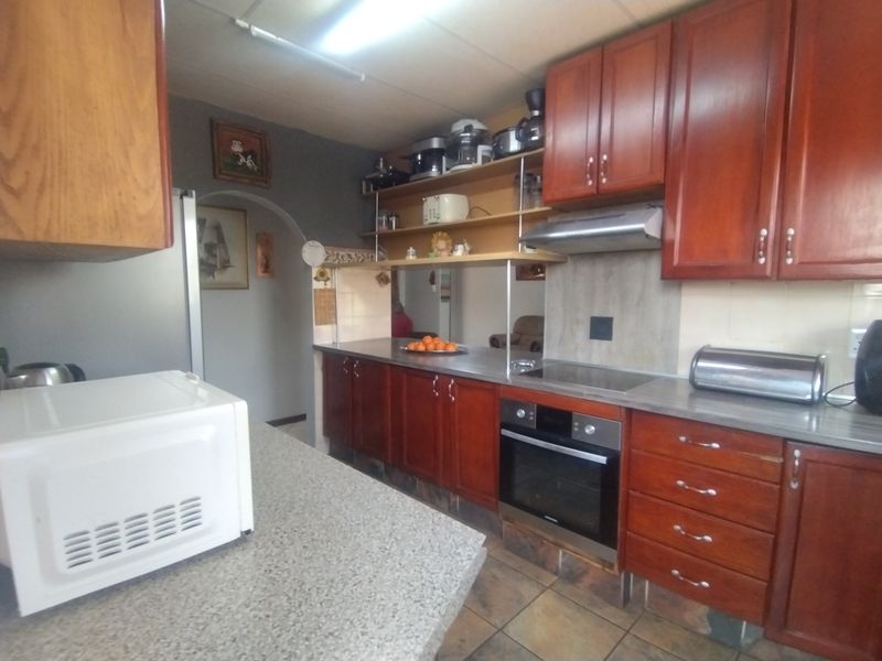 A functional kitchen featuring wooden cabinetry, built-in oven, electric hob, extractor fan, and laminate countertops with tiled flooring.