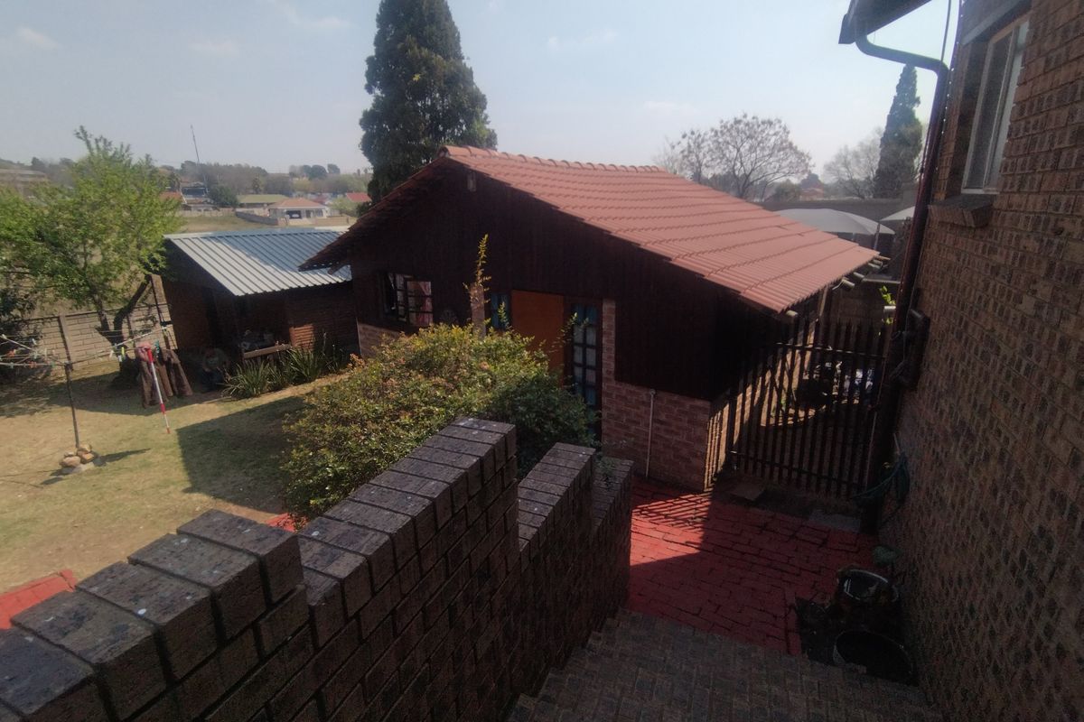 Rear exterior view of the townhouse property featuring a paved walkway, brick boundary wall, and secondary outbuilding structures in the garden area.