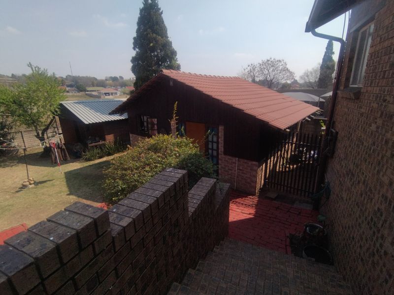 Rear exterior view of the townhouse property featuring a paved walkway, brick boundary wall, and secondary outbuilding structures in the garden area.