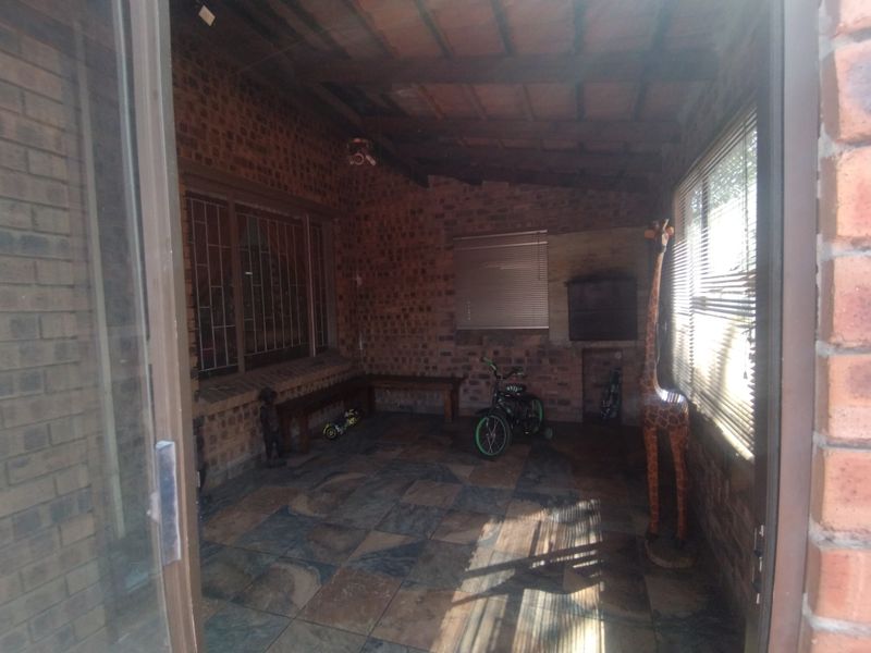 A covered patio area featuring exposed brick walls, tiled flooring, and a built-in braai, providing a functional outdoor entertainment space.