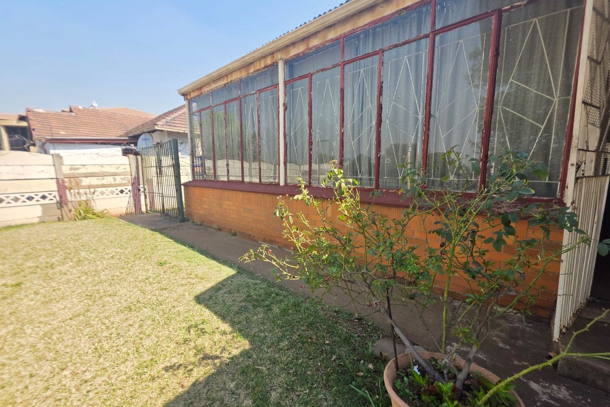 Rear view of the property featuring a brick facade, large metal-framed windows with security bars, and a concrete pathway leading to a garden area.