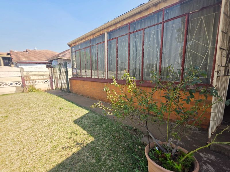 Rear view of the property featuring a brick facade, large metal-framed windows with security bars, and a concrete pathway leading to a garden area.