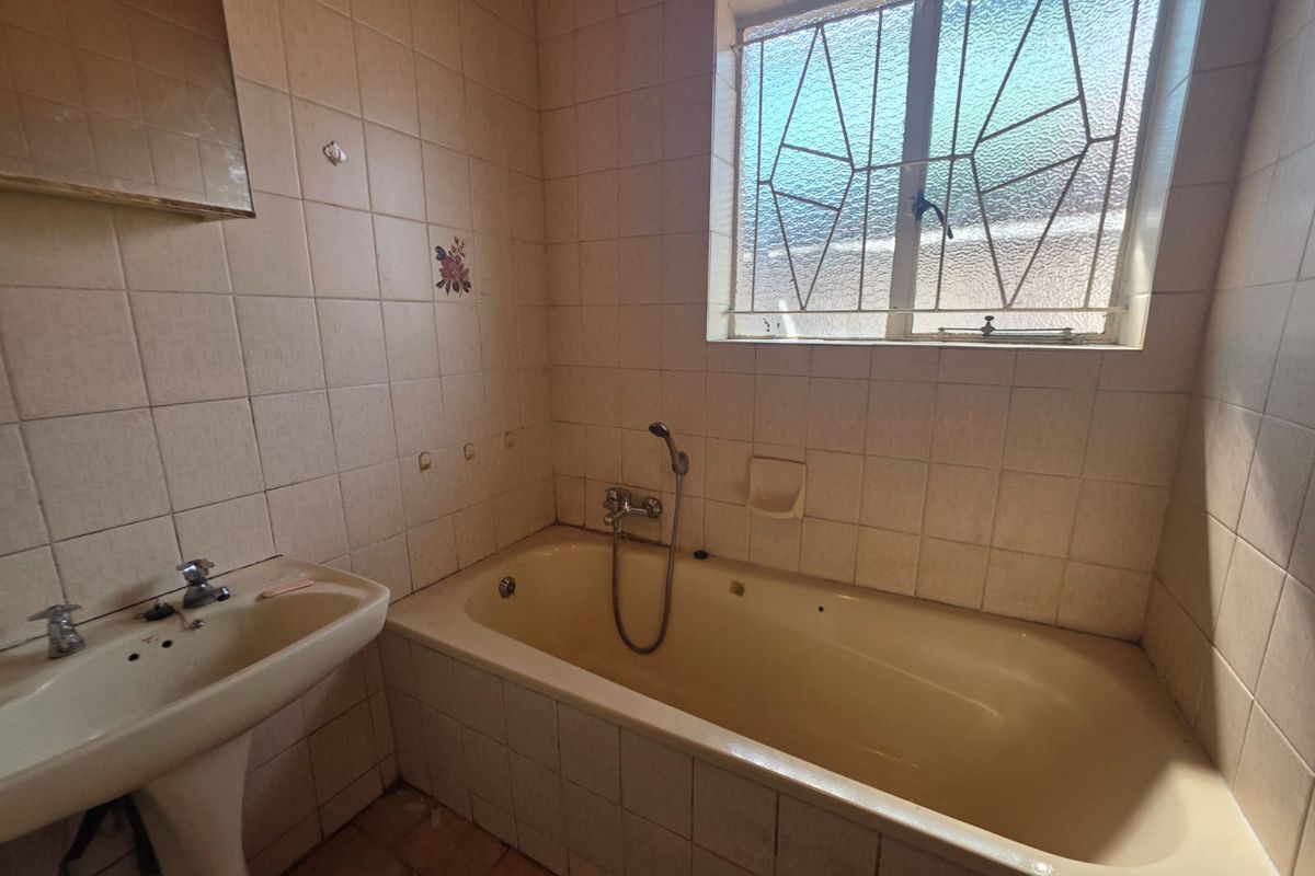 A dated bathroom featuring a pedestal basin and a built-in bathtub with tiled walls and security burglar bars on the window.