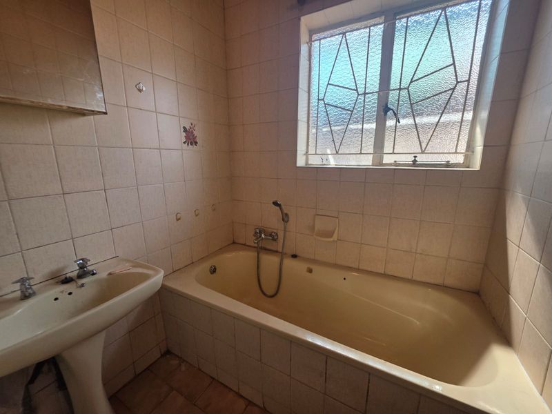 A dated bathroom featuring a pedestal basin and a built-in bathtub with tiled walls and security burglar bars on the window.