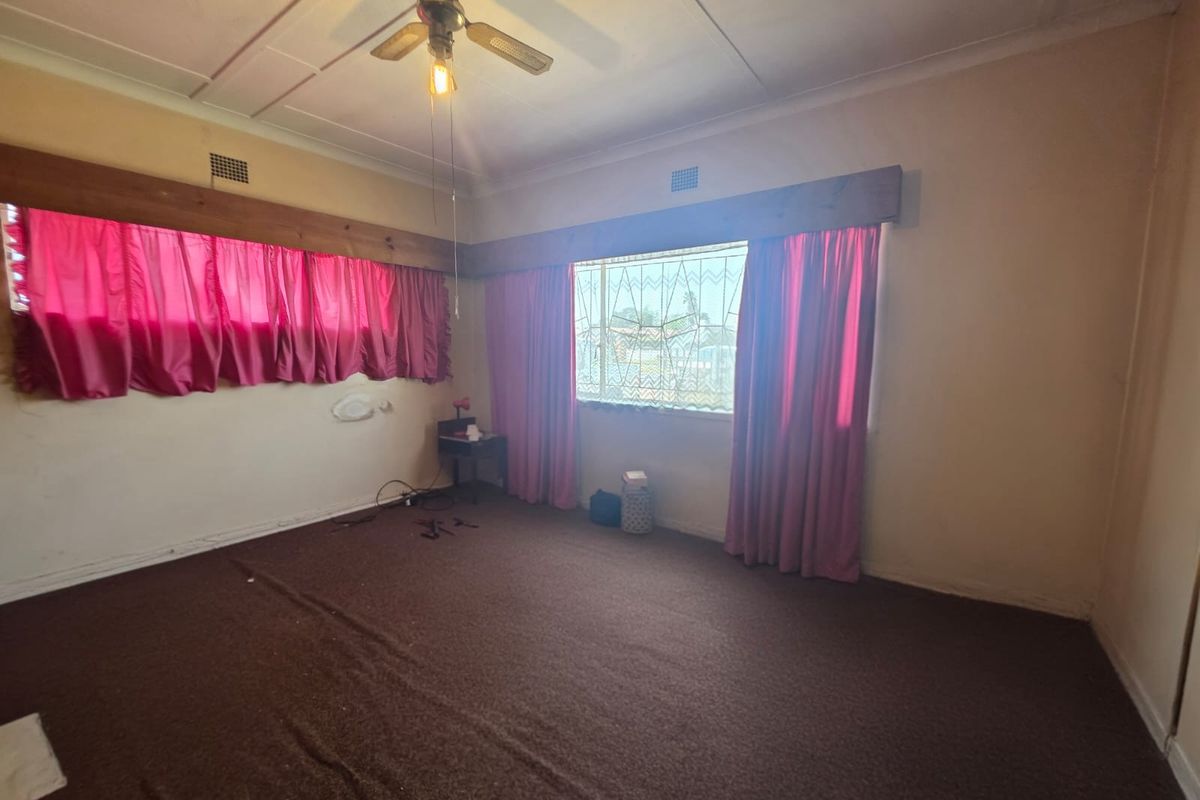 A vacant living room featuring a ceiling fan, security bars on windows, and dated wall-to-wall carpeting in need of refurbishment.