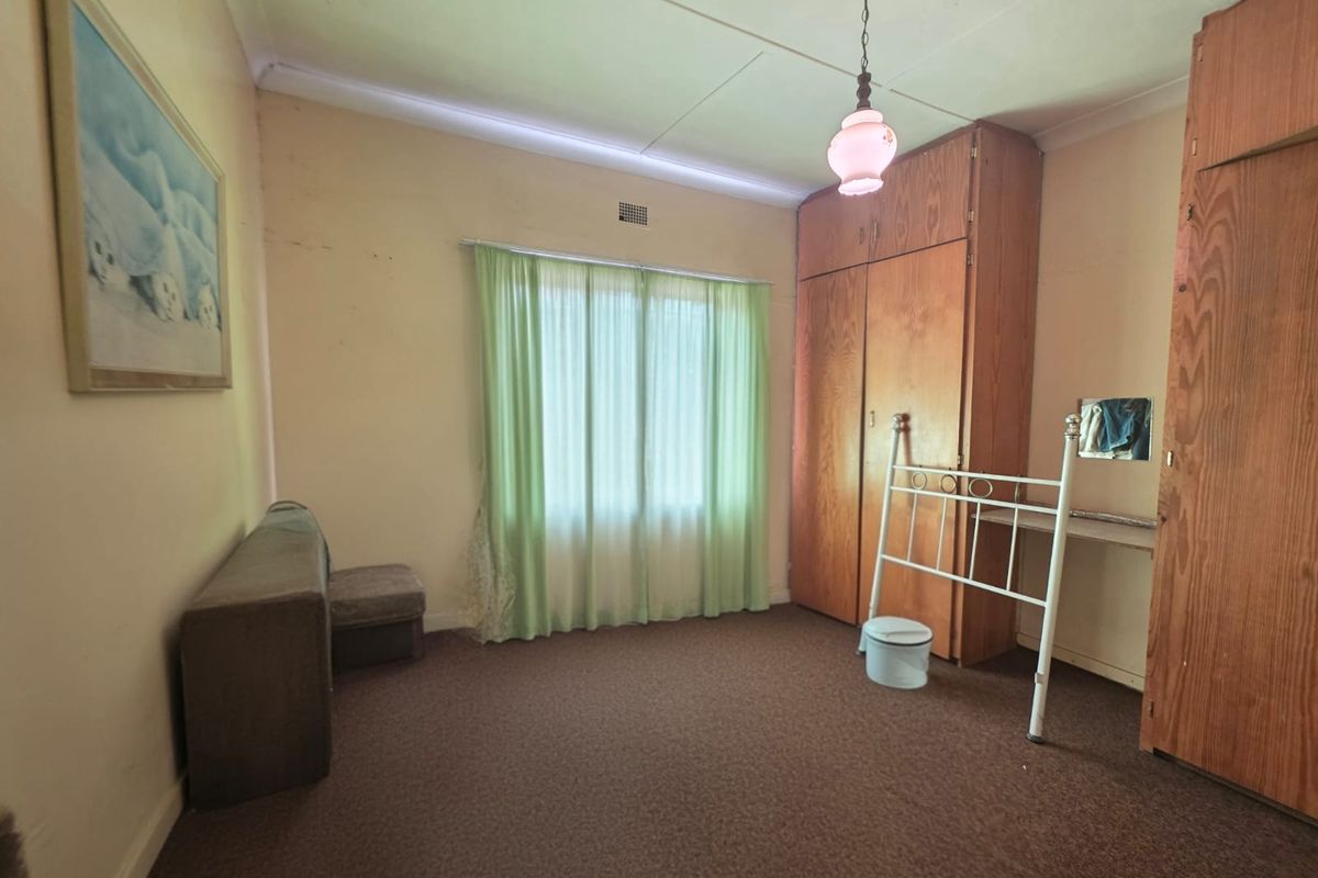 A bedroom featuring built-in wooden cupboards, carpeted flooring, and a pendant light fixture, offering a dated interior ready for modernization.