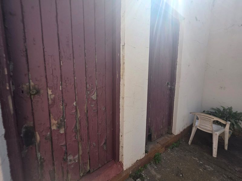 An outdoor utility area featuring two weathered timber doors and concrete paving, showing signs of significant wear and requiring maintenance.
