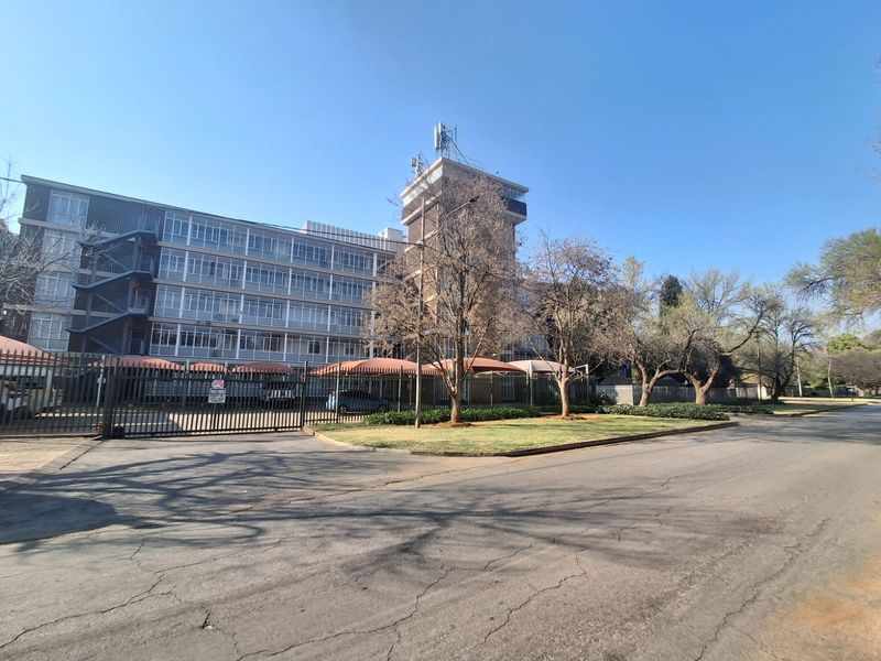 Exterior view of a multi-story apartment building featuring secure perimeter fencing, covered parking bays, and an external staircase.