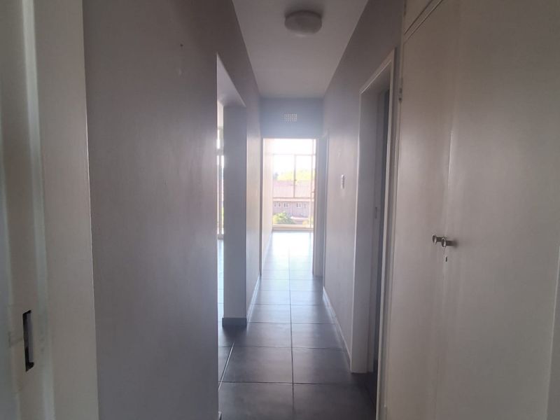 A clean, neutral hallway featuring tiled flooring and built-in storage cupboards, providing access to other areas of the flat.