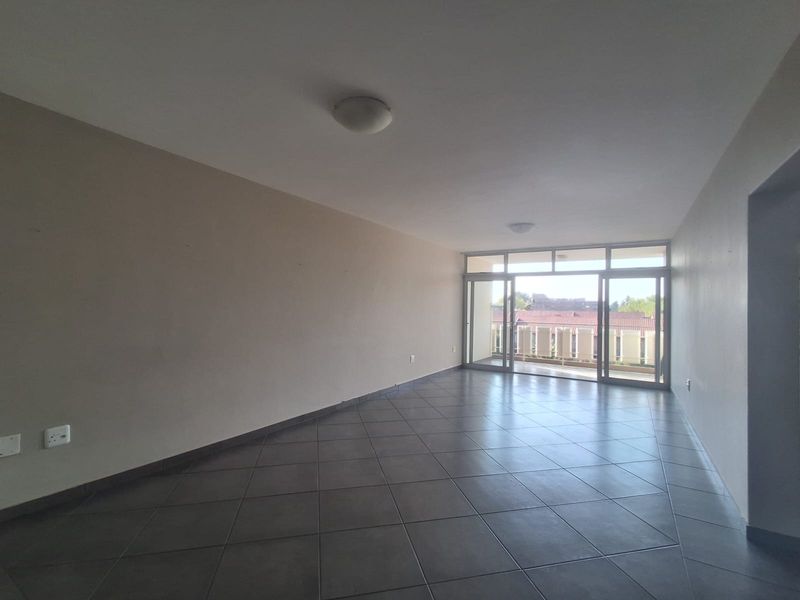 An empty, open-plan living area featuring dark tiled flooring and large sliding glass doors that provide access to an outdoor balcony.