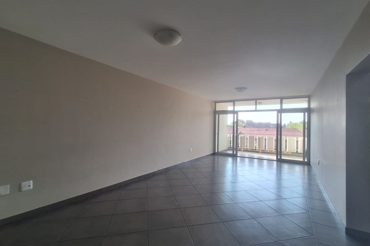 An empty, open-plan living area featuring dark tiled flooring and large sliding glass doors that provide access to an outdoor balcony.